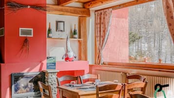 Un'accogliente sala da pranzo con mobili in legno, un camino in pietra e una finestra vista su una foresta innevata.
