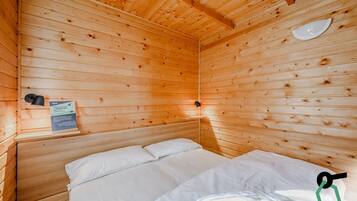 Une pièce de style cabane en bois, avec un lit, une lampe fixée au mur et un panneau accroché au mur.