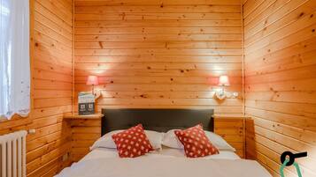 Una habitación acogedora tipo cabaña de madera con una cama, dos mesitas de noche y un letrero que indica una colección de habitaciones para festivos.