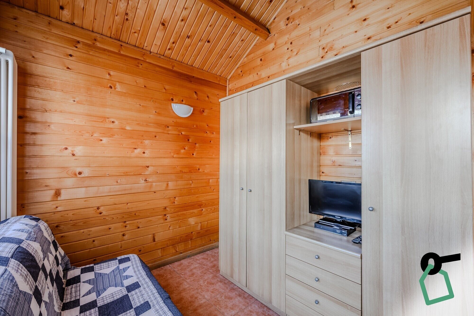 Ein Zimmer mit Holzwänden, einem Bett, einem integrierten Fernseher und einer Kommode mit Schubladen.