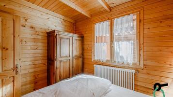 Une chambre dans un chalet en bois, avec un lit, une armoire et une fenêtre ornée de rideaux en dentelle.