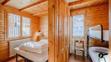 Habitación de cabaña de madera con una cama individual, una litera, una silla y un radiador.
