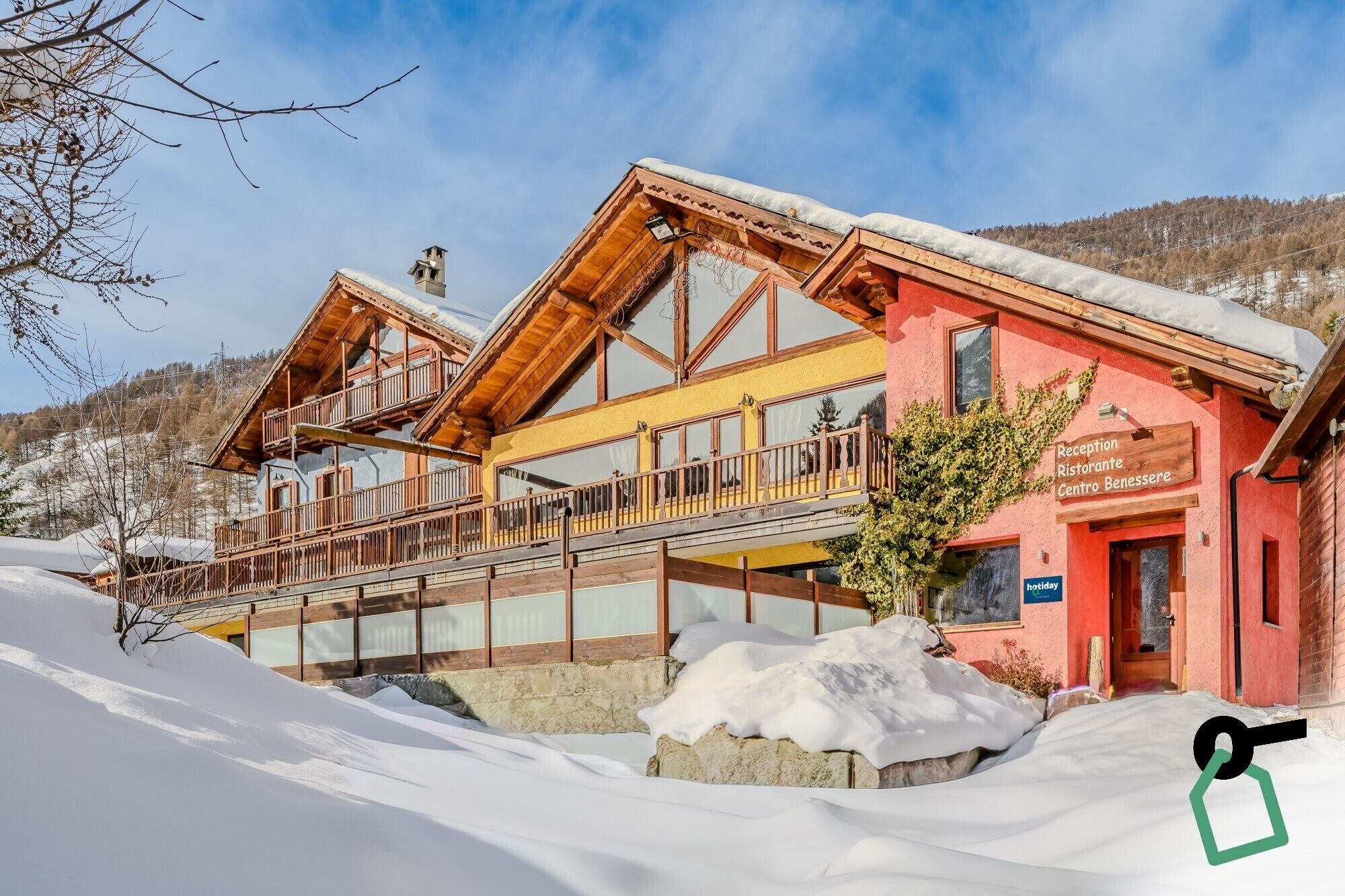 Ein zweistöckiges Holzhaus mit Balkonen und einer roten Fassade, umgeben von Schnee.
