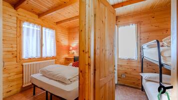 Una habitación de cabaña de madera con una cama litera, una cama individual y un radiador.