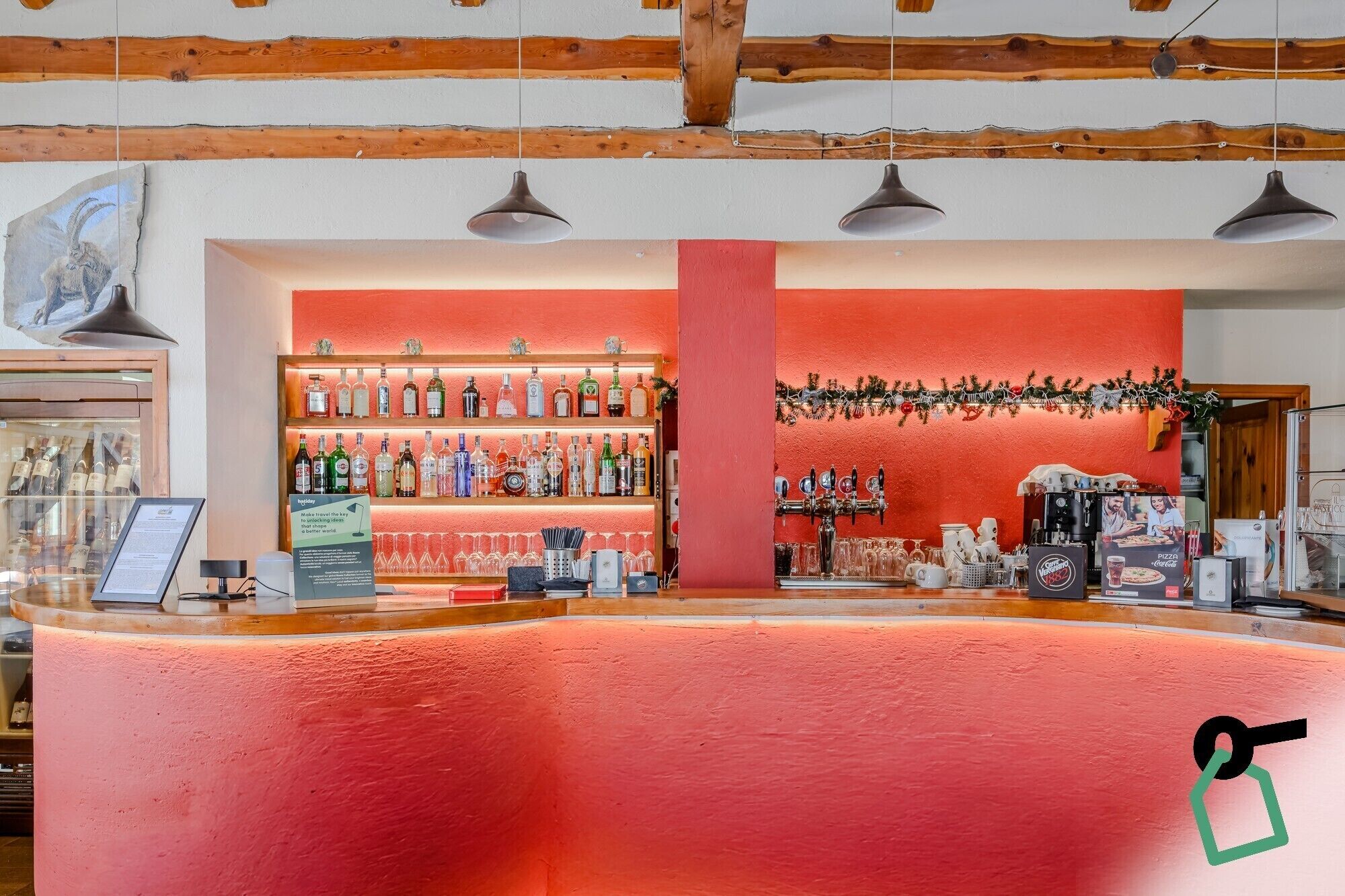 Una zona de bar con una barra roja, estantes con botellas de licores y una máquina de café.