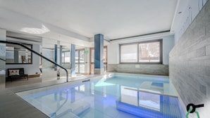 A modern indoor swimming pool with clear glass walls, a bench, and a staircase. - Hotiday Pragelato (Pragelato)