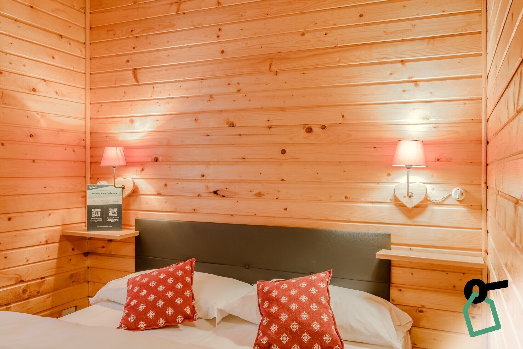 Ein Zimmer einer Holzhütte mit einem Bett, zwei Nachttischen, einer Lampe und einer Wanddekoration in Herzform.