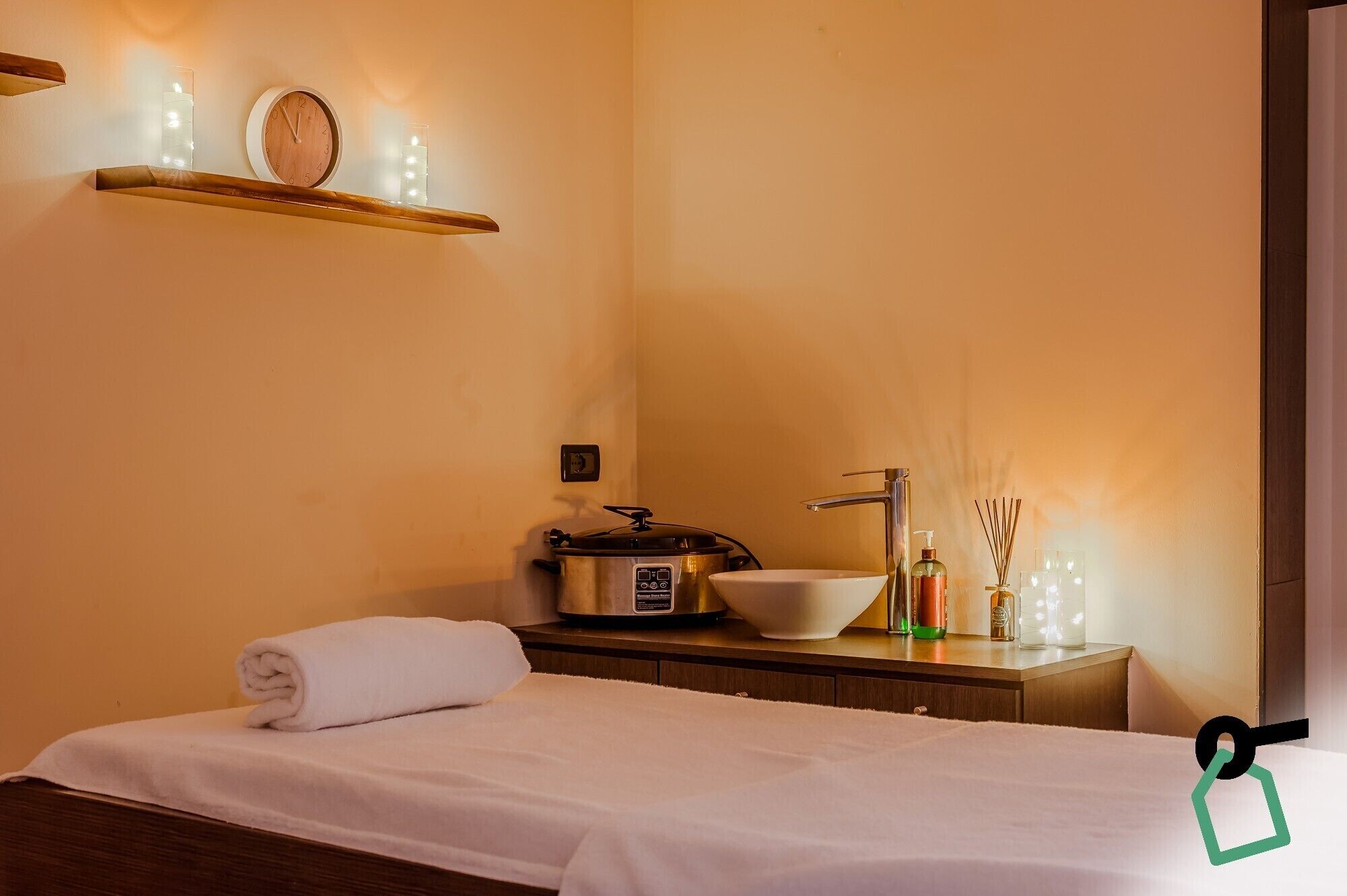 A hotel room with a bed, a bedside table with a lamp, a sink, and a small shelf with decorative items.