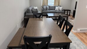 A modern living room with a wooden dining table, two sofas, and a large window with curtains. - Relaxing Modern 3BR Condo (Harrisburg)