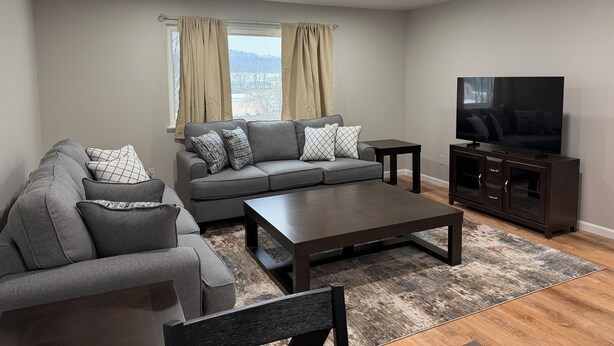 A modern living room with a grey sofa, a coffee table, and a TV on a wooden cabinet. - Relaxing Modern 3BR Condo (Harrisburg)