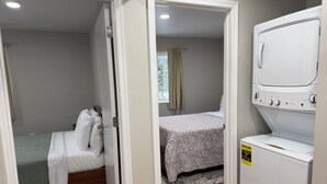 A bedroom with a bed, a second bed, and a washing machine. - Relaxing Modern 3BR Condo (Harrisburg)