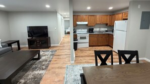 A modern kitchen with wooden cabinets, a white refrigerator, and a stove. There is a dining area with a table and chairs. - Relaxing Modern 3BR Condo (Harrisburg)