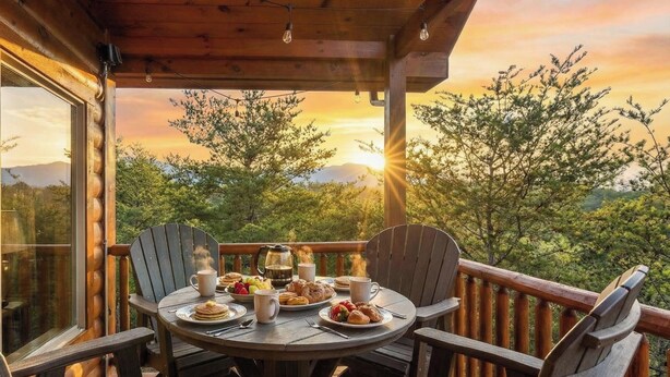 Eine Holzdielen-Terrasse mit einem für das Frühstück gedeckten Tisch, mit Blick auf eine malerische Landschaft aus Bäumen und Bergen.