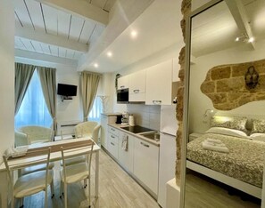 A modern hotel room with a kitchen area, a dining table, and a bed with a stone accent wall. - Protea House 2 - Alghero (Alghero)