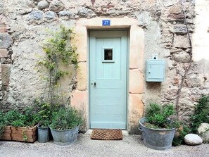 A rustic stone building with a light blue door, numbered 27. There are potted plants and a small wooden bench outside. - Bright, Cozy Apartment (Génolhac)