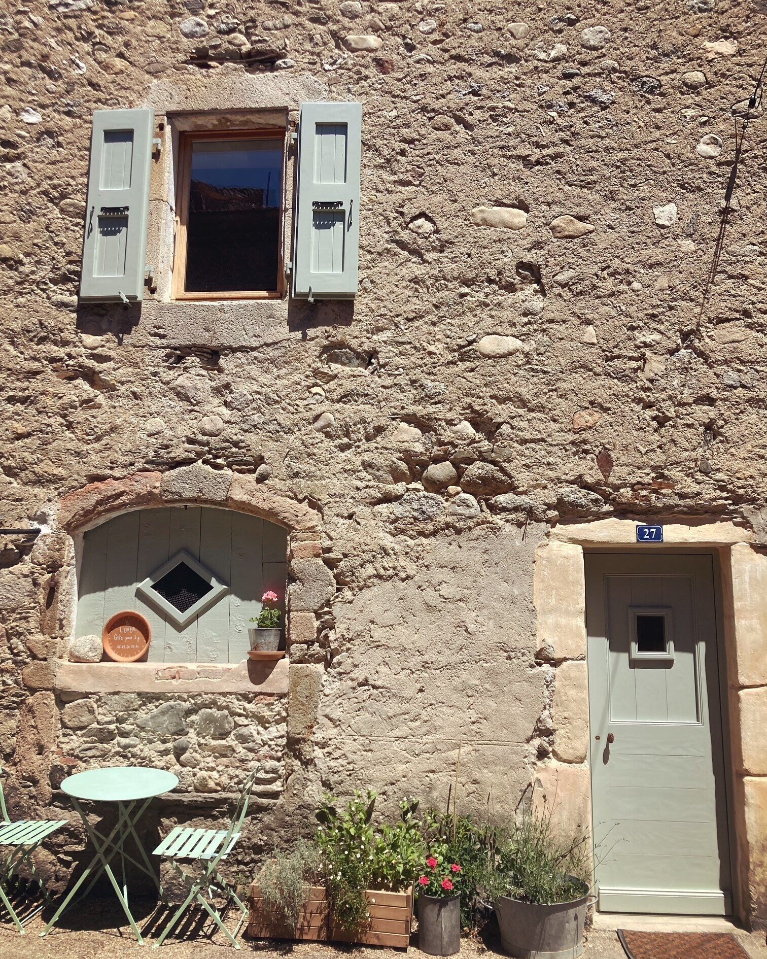 Un edificio de piedra rústico con una ventana pequeña, una puerta y una mesa con sillas afuera.