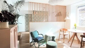 Ein modernes Wohnzimmer mit Holzboden, einem grünen Schaukelstuhl, einem kleinen runden Tisch und einer weißen Lampe.