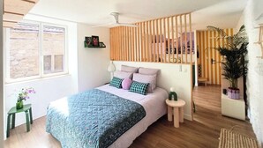 Ein Schlafzimmer mit Bett, Fenster, einer Holzwand, einem kleinen Tisch und einem Blumentopf.