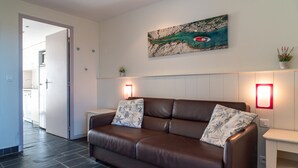 A modern living room with a brown leather sofa, two matching pillows, a wall-mounted painting, and two wall sconces. - Sud Ocean M Ndeg105 - 2P5 (Guidel)