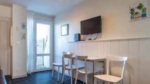 A modern kitchen with a flat-screen TV, white chairs, and a dining table. - Sud Ocean M Ndeg105 - 2P5 (Guidel)