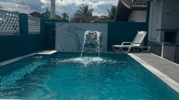 Une piscine agrémentée d’un élément décoratif aquatique, entourée d’une clôture et bordée d’un bâtiment dont le toit est recouvert de tuiles.