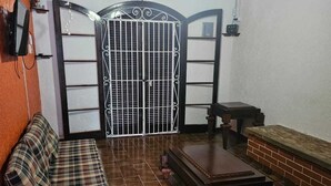 Une pièce avec un canapé à carreaux, une table en bois, un banc en briques et un portail en métal orné d’une croix.