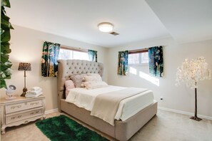 Un dormitorio con cama de cabecera capitonada, alfombra mullida verde, mesita de noche con lámpara y una lámpara de pie.