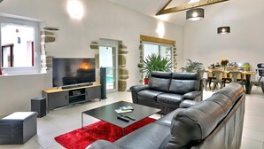 Ett modernt vardagsrum med en tv, lädersoffor, en röd matta och en matplats med ett bord och stolar.