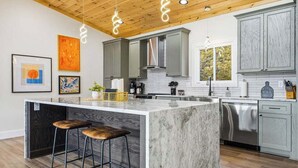 Una cocina moderna con una isla de mármol, taburetes de bar y techo de madera.