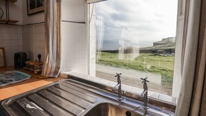 Eine Küche mit einer Edelstahlspüle, einem Fenster mit Blick auf ein grasbewachsenes Feld und ein entferntes Gebäude, sowie einem Bild an der Wand.