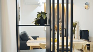Ein modernes Wohnzimmer mit Essbereich, mit einem Bücherregal mit schwarzem Rahmen, einer Topfpflanze, einer Couch und einem Fernseher.