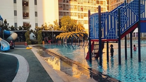Ein Spielbereich für Kinder mit Rutsche und Klettergerüsten, ein Pool mit Wasserspielen sowie ein Gebäude im Hintergrund.
