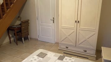 Quarto com escada, porta branca, guarda-roupa, mesinha com abajur e tapete estampado.