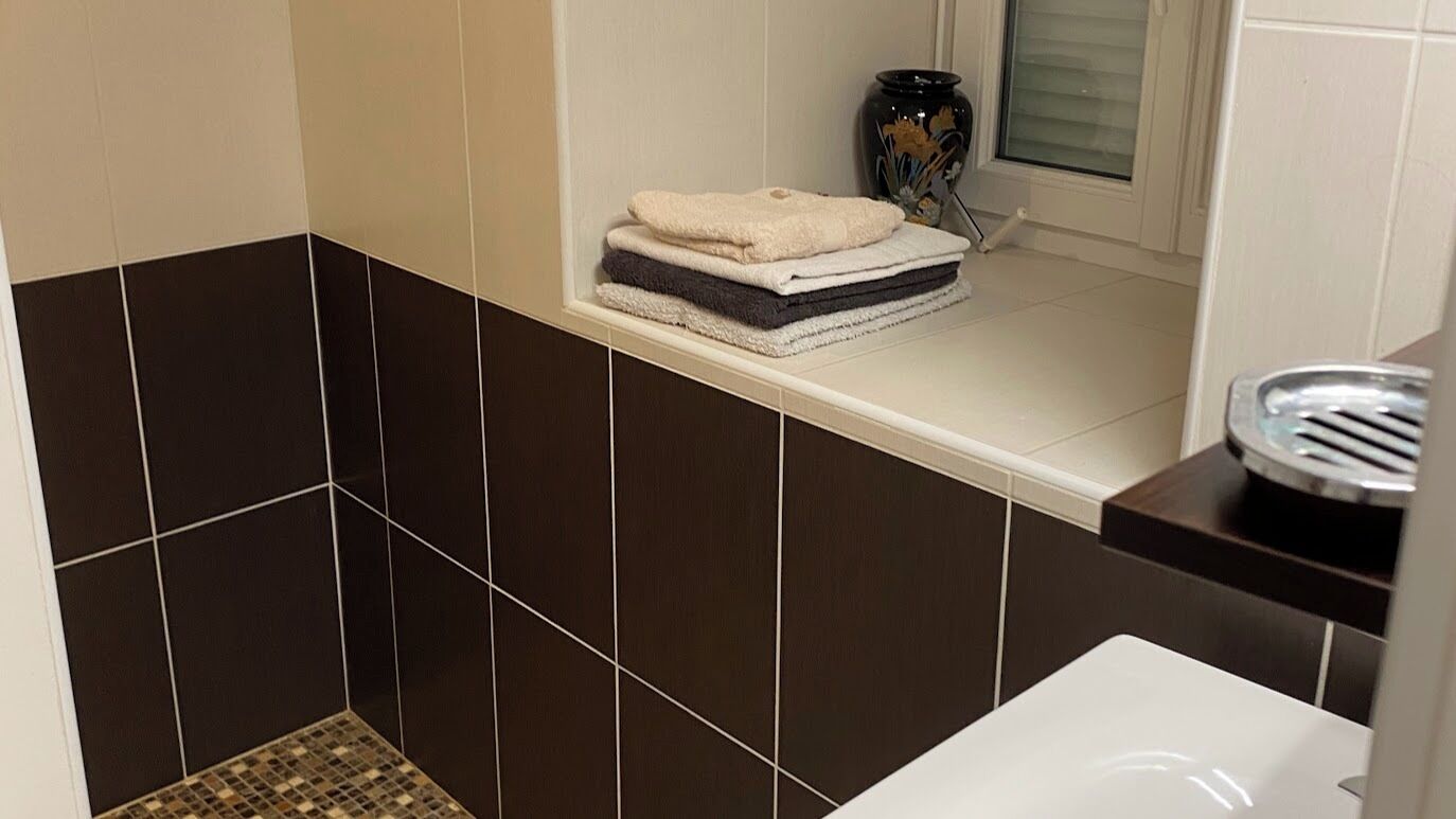 Een badkamer met donkerbruine tegels, een witte wastafel en een raam met een decoratieve vaas.