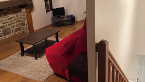 Ett vardagsrum med en röd soffa, ett träbord, en steneldstad och en tv som står på ett stativ.