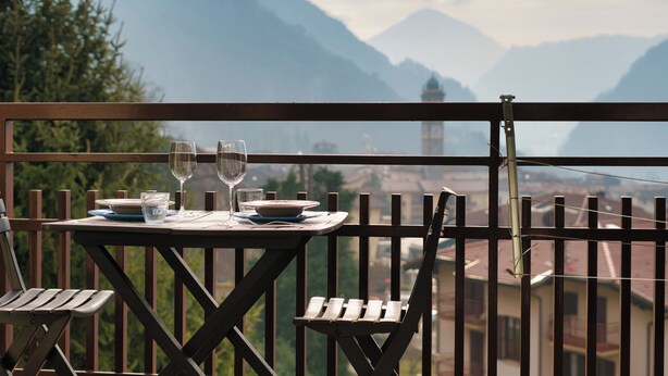 Ein Tisch mit Geschirr, Gläsern und Besteck auf einem Balkon mit Blick auf die Berge.