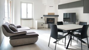 Ein modernes Wohnzimmer mit grauem Sofa, einem Esstisch mit Stühlen, einem Kamin und einem an der Wand befestigten Fernseher.