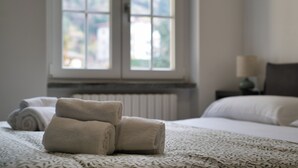 Ein ordentlich bezogenes Bett mit aufgerollten Handtüchern, ein Fenster mit Blick und ein Nachttisch mit Lampe.