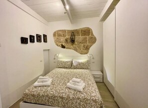 A bedroom with a large bed, a stone wall, and framed pictures on the wall. - Protea house 1 - Alghero (Alghero)