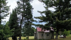 Une maison avec un toit rouge, entourée d’une cour verdoyante et de grands arbres.