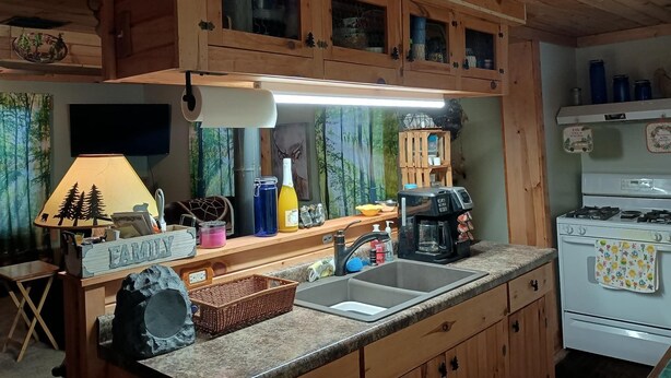 Une cuisine avec des meubles de rangement en bois, un évier, une cuisinière et divers ustensiles de cuisine.