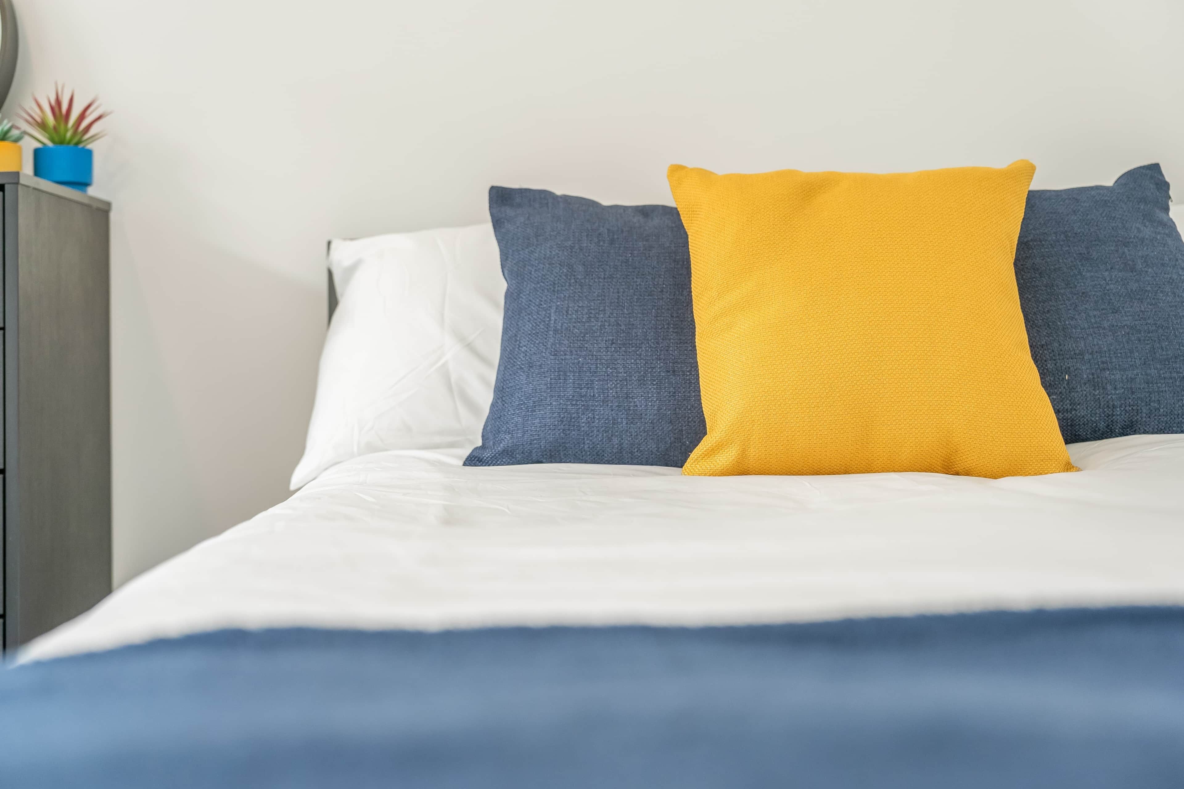 A bed with white sheets and two pillows, one blue and one yellow.