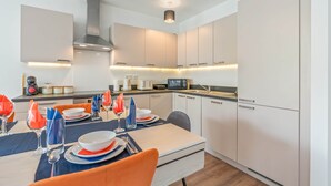 A modern kitchen with white cabinets, a stainless steel range hood, and under-cabinet lighting. - Wembley Stadium | Luxury London Apartment | Balcony Views, Netflix, Pool Table! (Wembley)