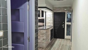 A hallway with a modern design, featuring a stone accent wall, a black door, and a kitchen area with a countertop. - Prestige Apartment & 24h Security (Ouled Fayet)