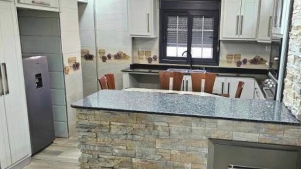 A kitchen with a stone island, white cabinets, and a refrigerator. - Prestige Apartment & 24h Security (Ouled Fayet)