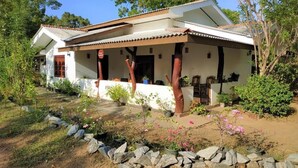 A two-story house with a covered porch, surrounded by a garden with various plants and a stone pathway. - lavish eco jungle (Weerawila)