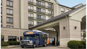 Um ônibus de transporte azul e laranja estacionado em frente a um hotel Hyatt Place com entrada coberta e fachada de tijolos.
