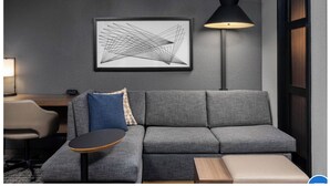 Uma sala de estar moderna com um sofá cinzento, uma mesa redonda pequena, um abajur e uma obra de arte abstrata emoldurada na parede.