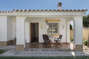 A covered patio with two chairs and a table, a window with bars, and a door leading inside. - Rural House 'Casas Pepe 1' with Private Terrace, Wi-Fi and Air Conditioning (Los Caños de Meca)