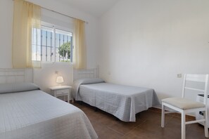 A room with two beds, a chair, a nightstand with a lamp, and a window with curtains. - Rural House 'Casas Pepe 1' with Private Terrace, Wi-Fi and Air Conditioning (Los Caños de Meca)